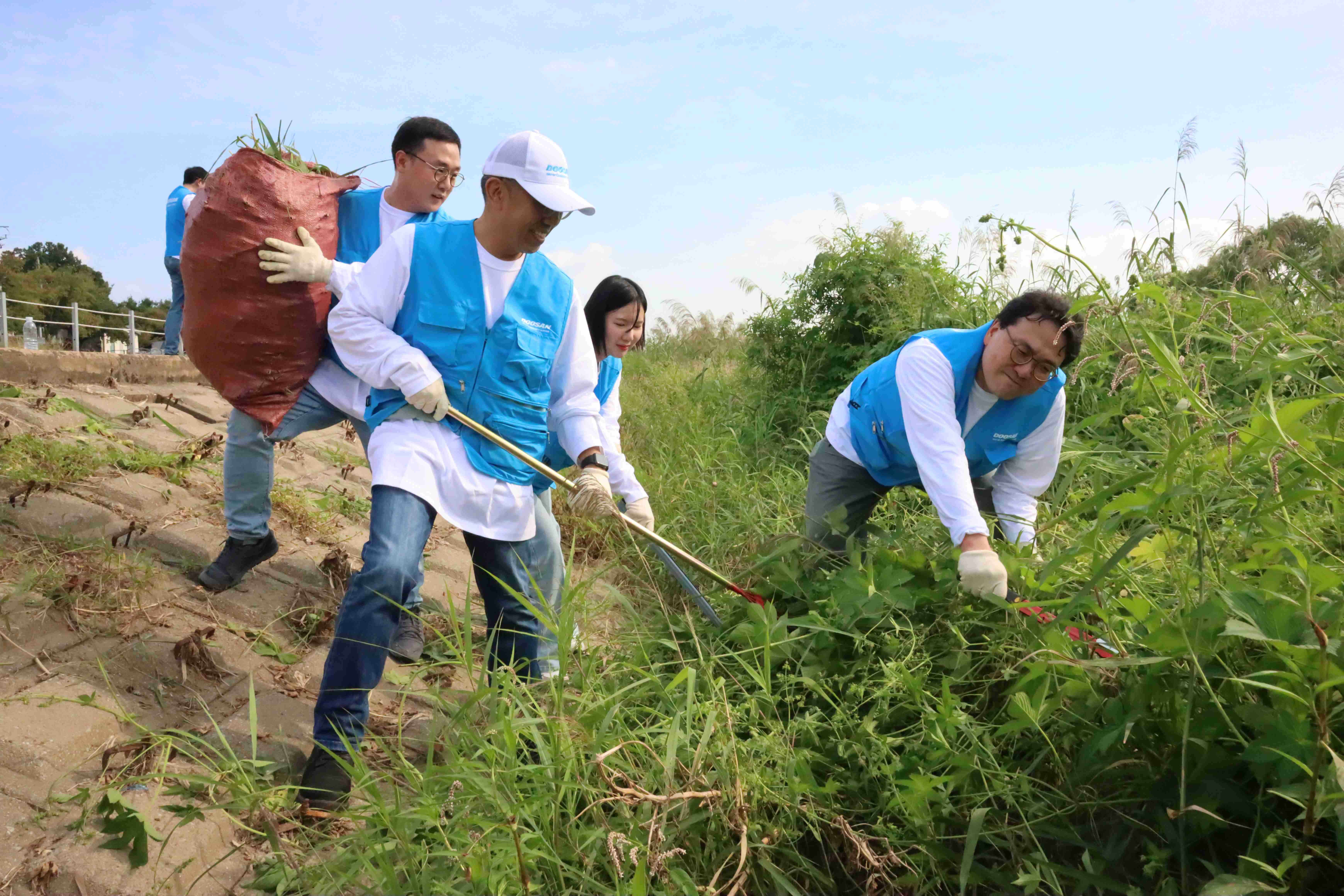 두산밥캣 임직원들이 경기도 성남시에서 탄천 주변의 유해식물 ‘환삼덩굴’ 제거 작업을 하고 있다.